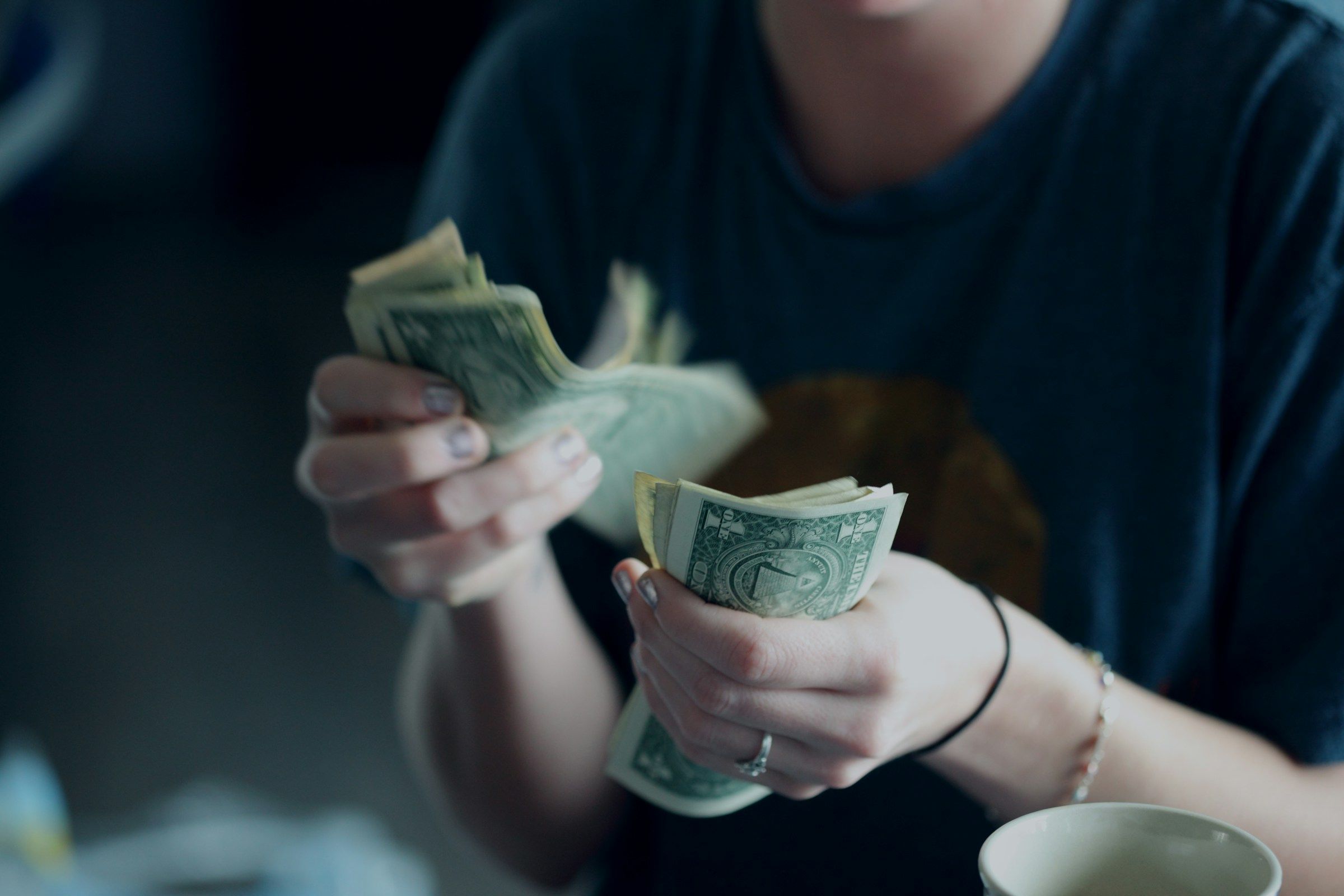 A person counting dollar bills beside a coffee cup