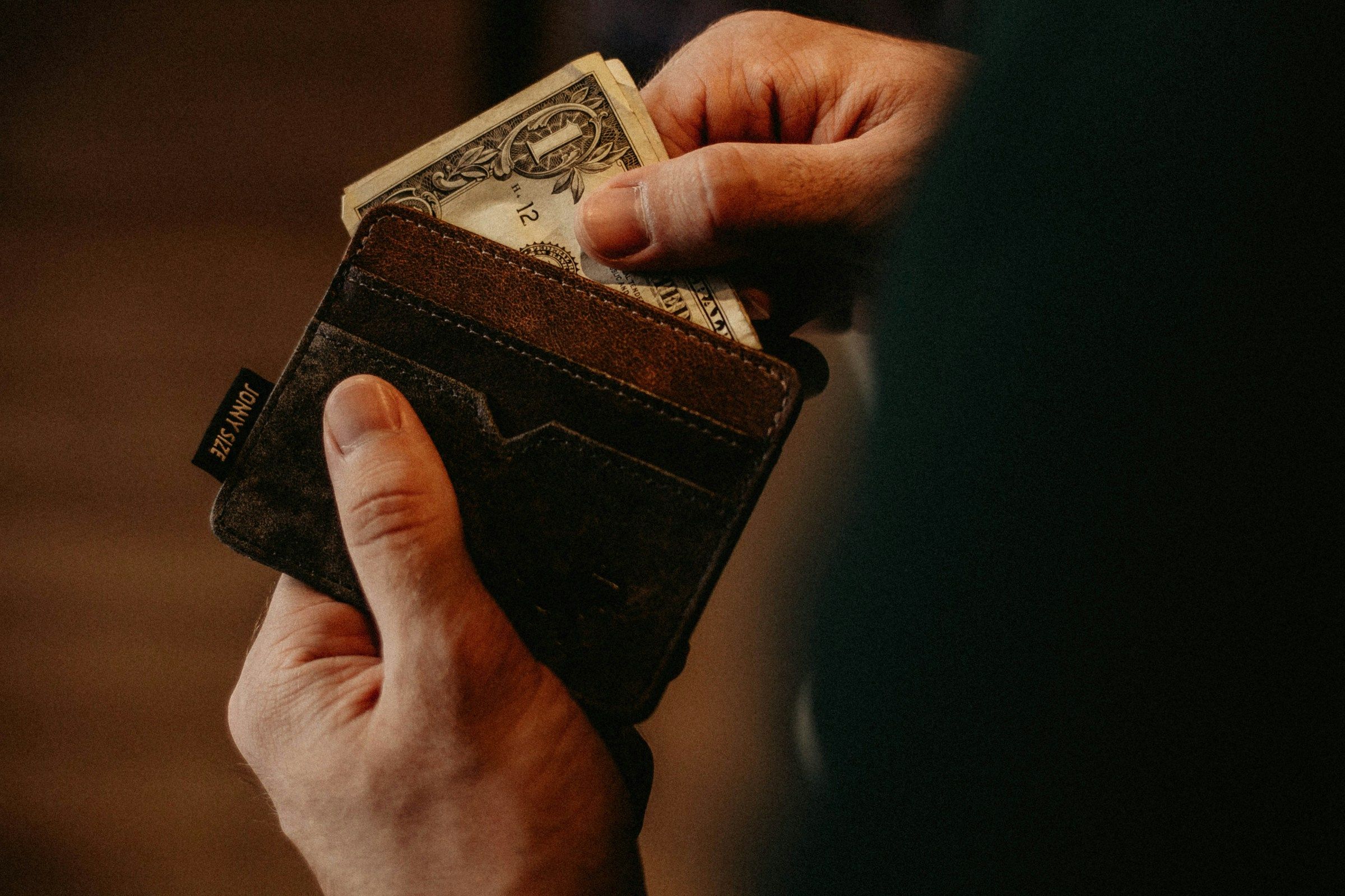 A person placing a one-dollar banknote into a wallet