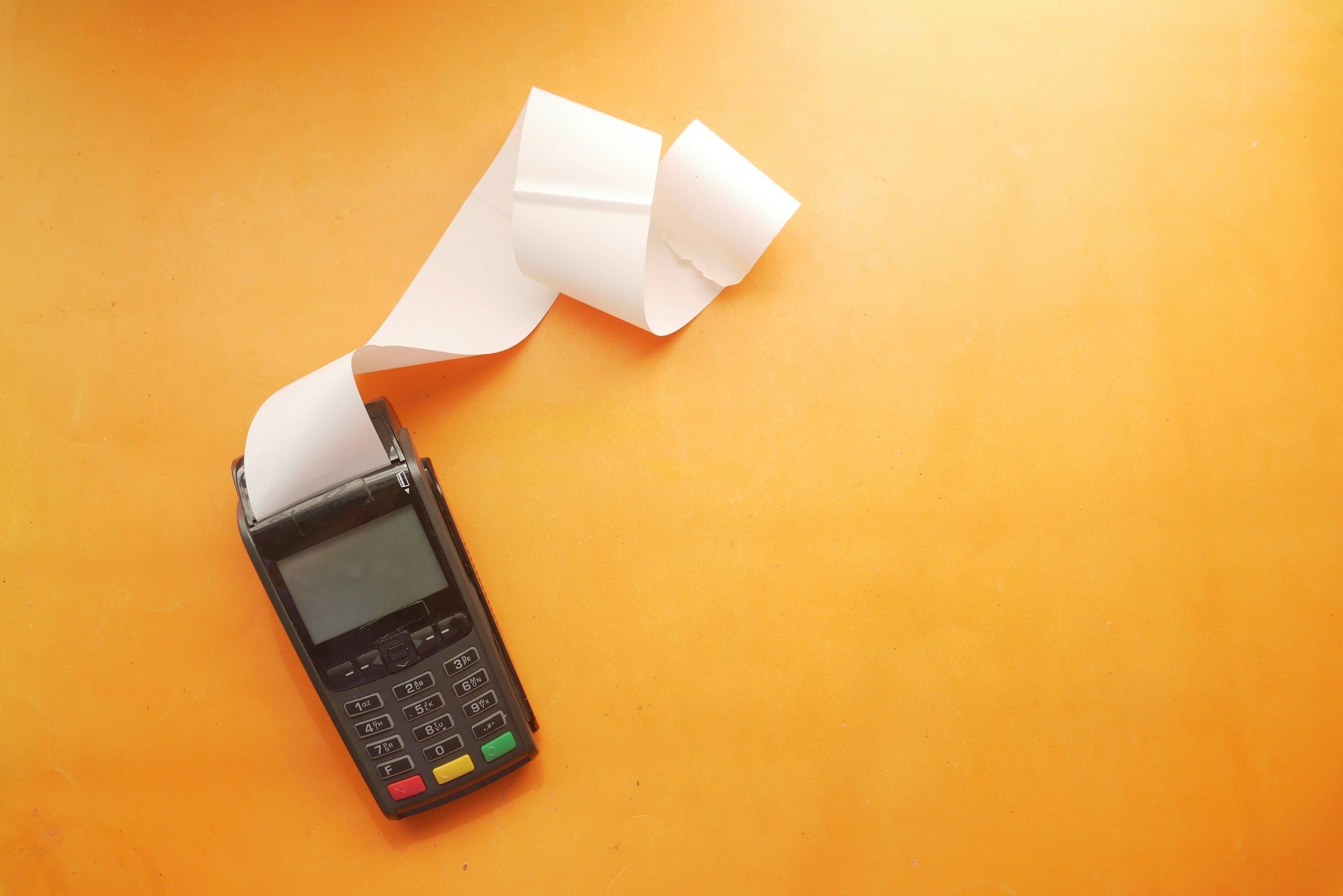 A black payment terminal with a long white receipt on an orange background