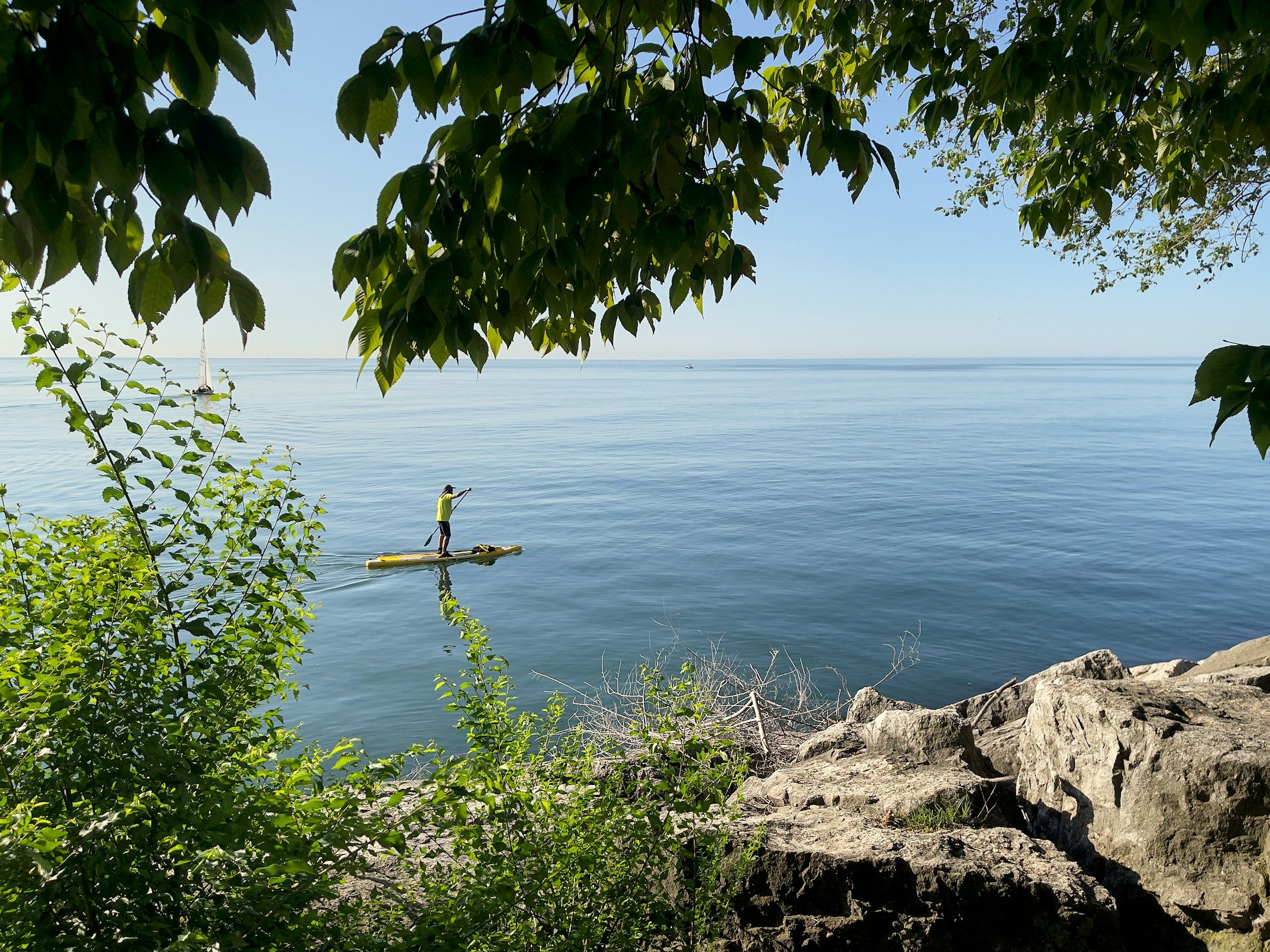 A person paddleboarding on calm Lake Ontario under a blue sky