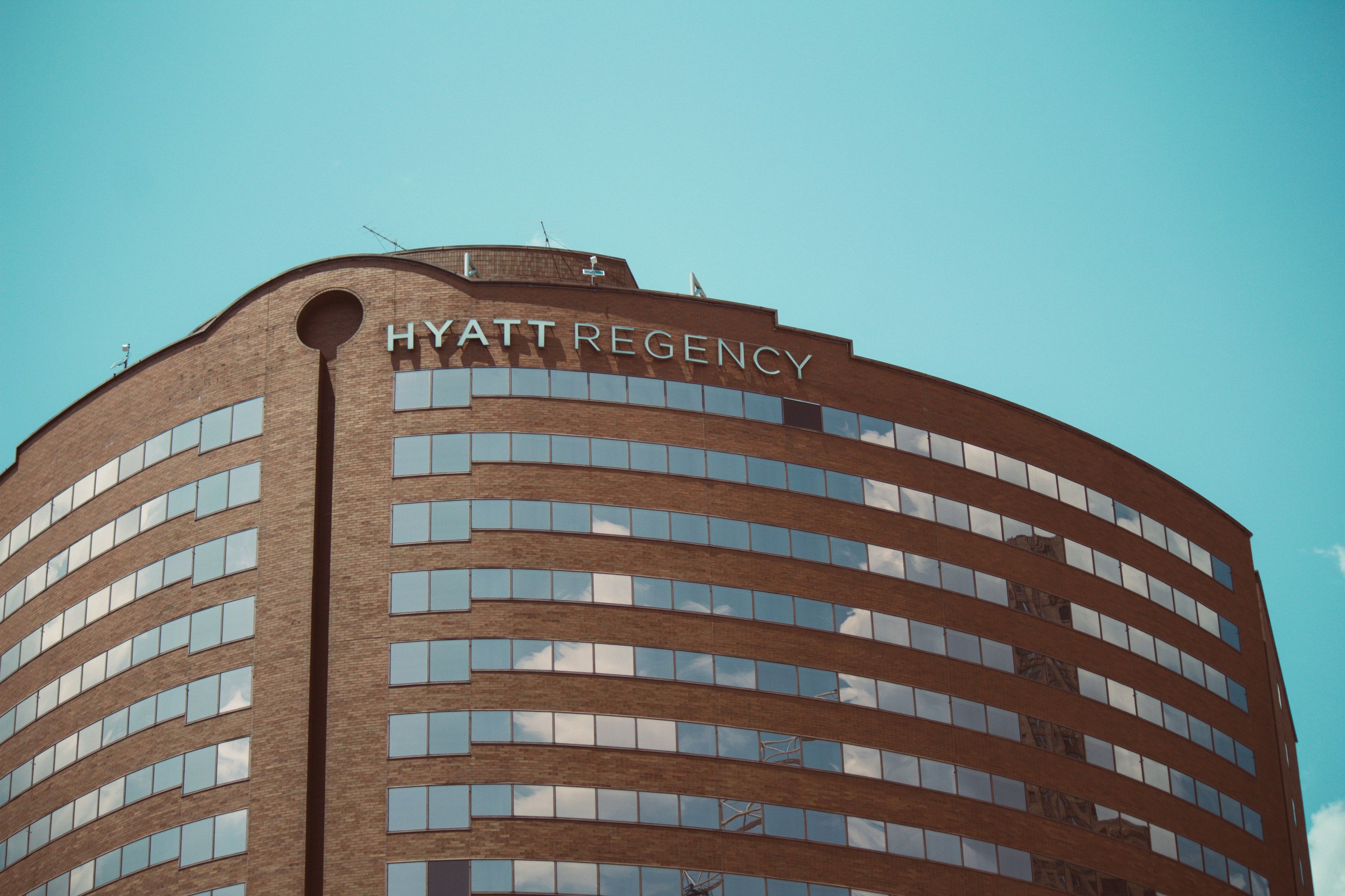 Curved brick Hyatt Regency hotel facade beneath a turquoise sky.