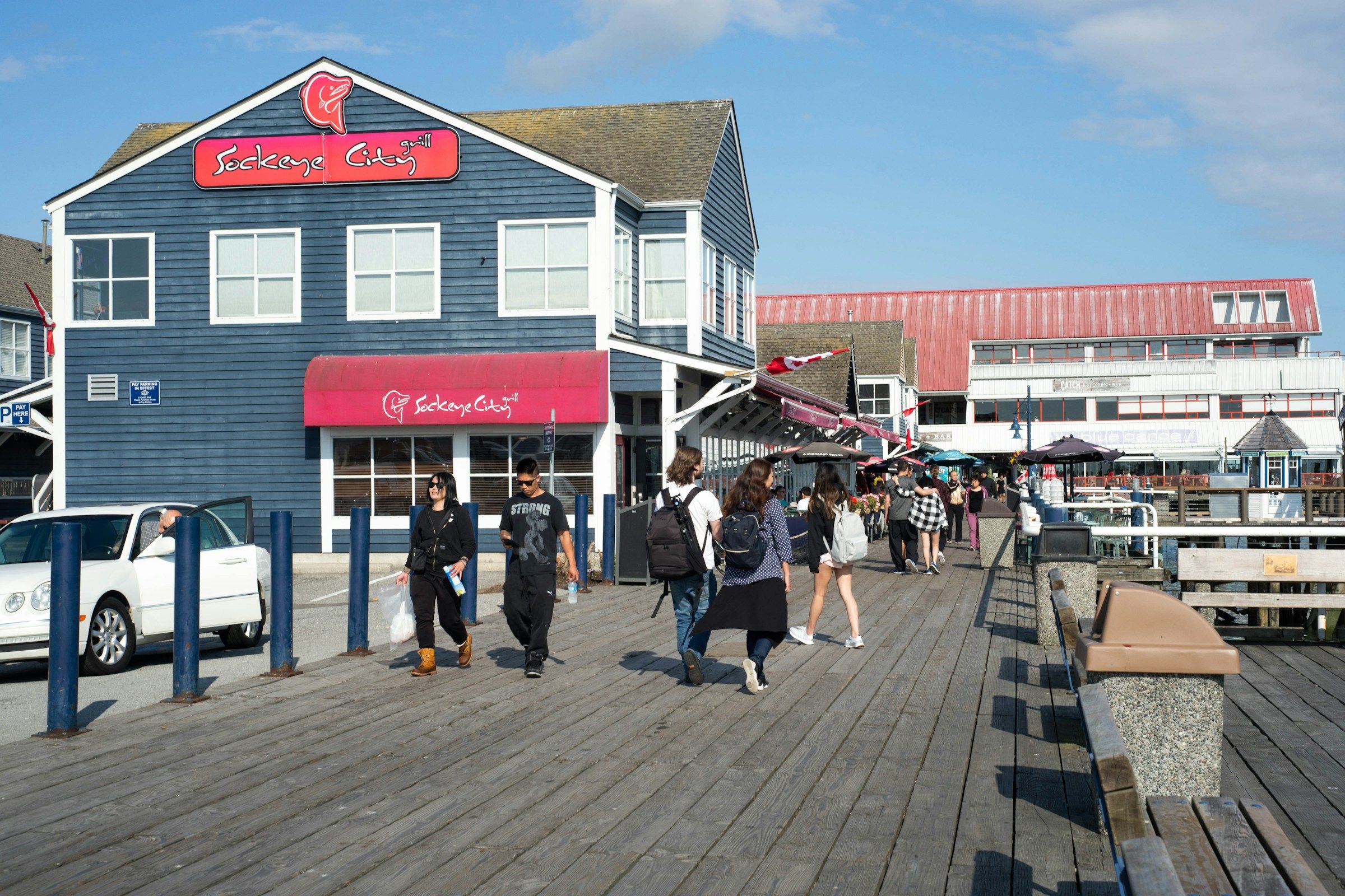 People walking along a wooden boardwalk beside fishing boats at a dock in British Columbia