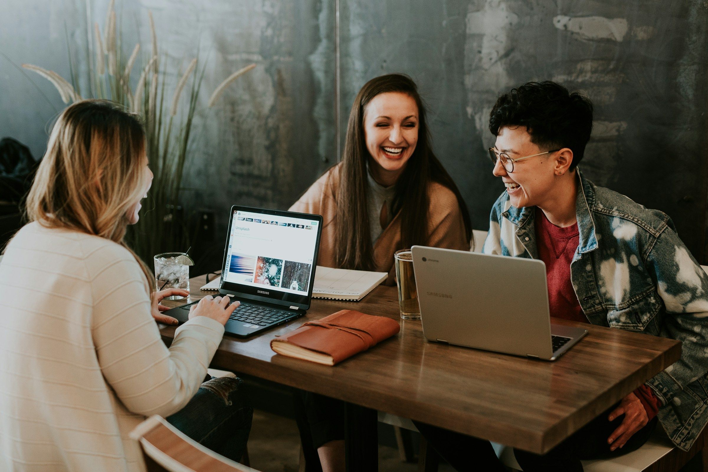 Three people laughing together around a table with a laptop
