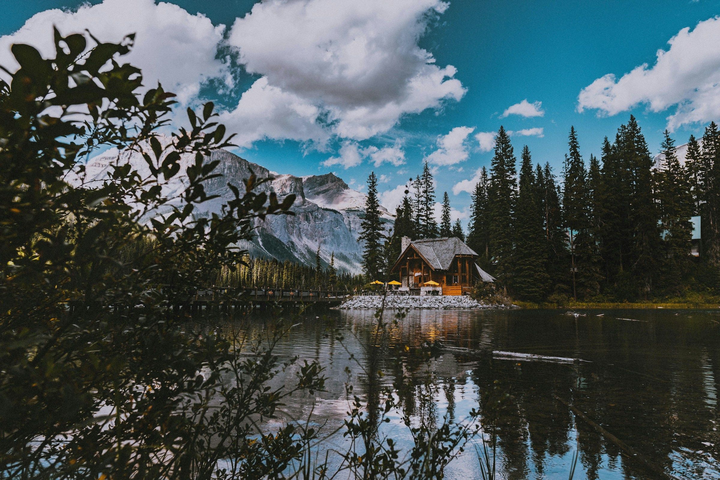 Brown wooden cabin beside a green forest and mountain lake in British Columbia
