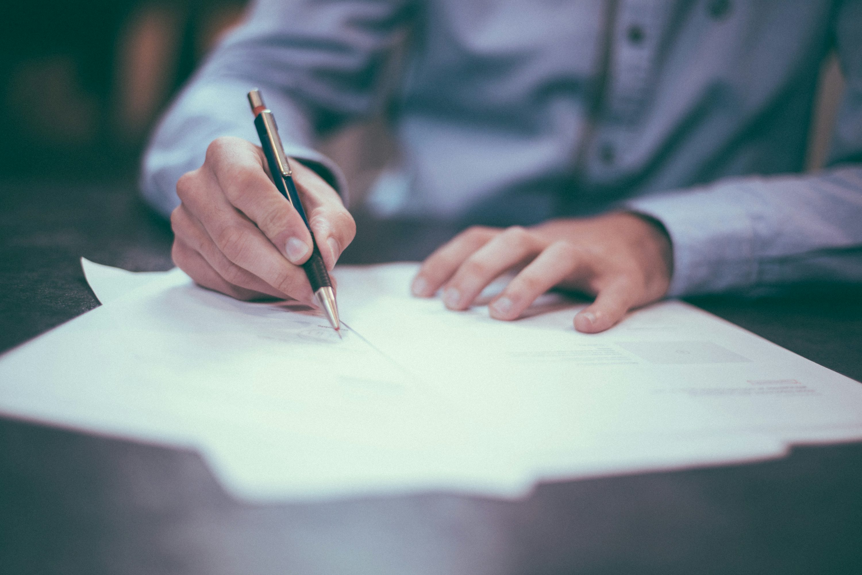 Person writing on a paper income document at a desk.