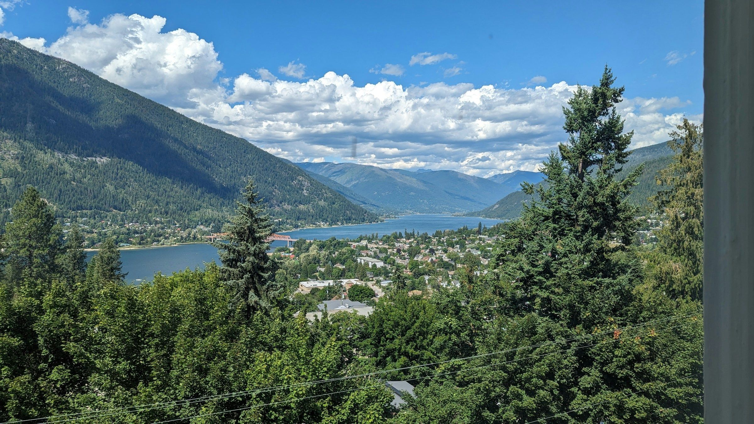 A town on a forested hillside beside a large lake surrounded by mountains