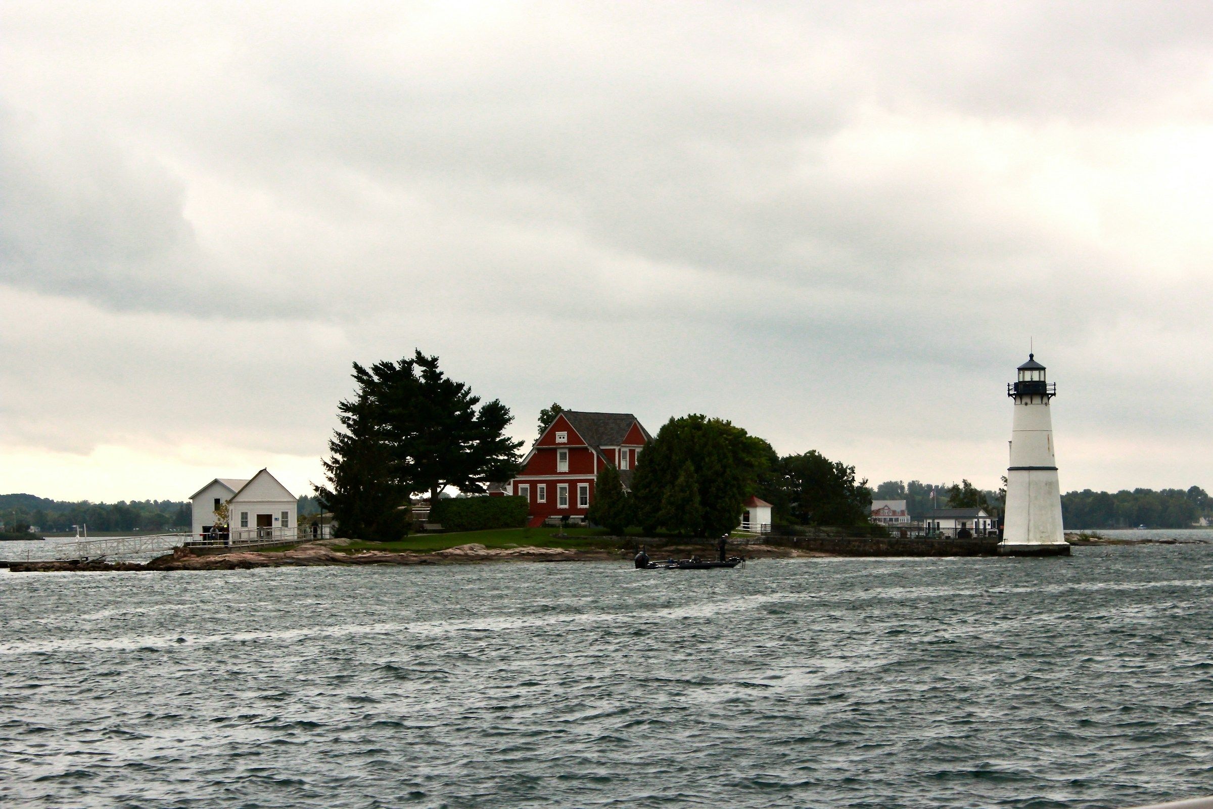 A boat passing a small island with a lighthouse and a house on the St. Lawrence River