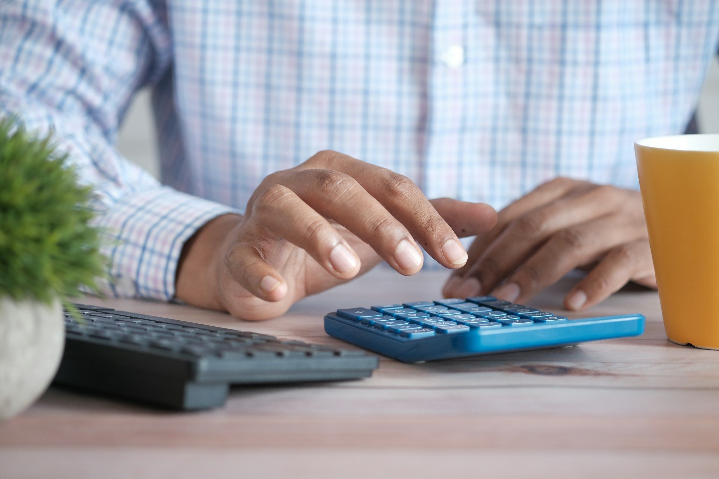 Person using a calculator at a desk beside a coffee mug