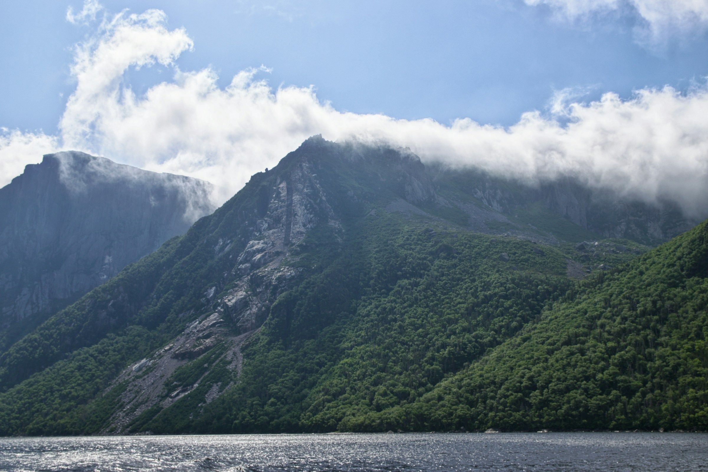 Cliffs rising from a long freshwater fjord with clouds rolling over the plateau above
