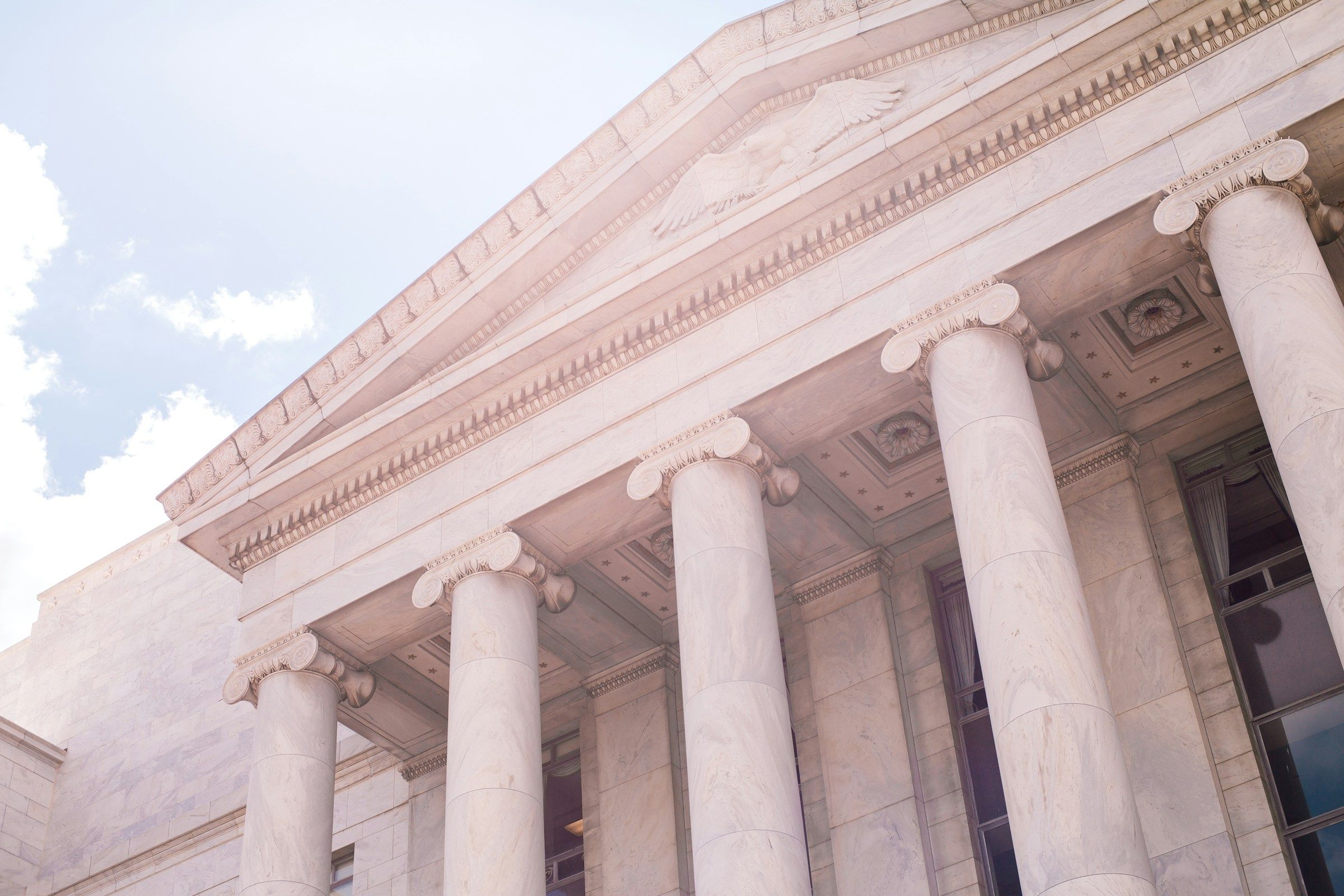 Sunlit government building with tall white stone columns beneath a pale blue sky